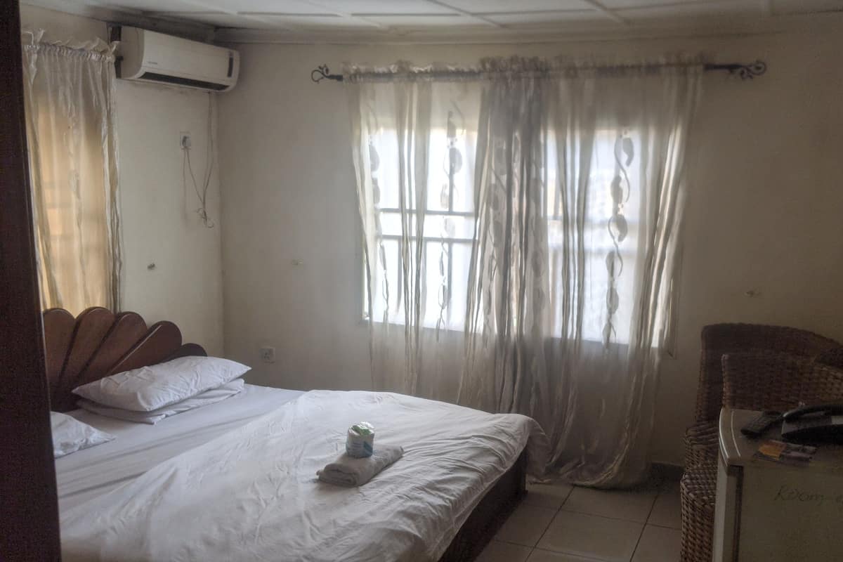 A bedroom with a bed, a television, and a window with curtains.