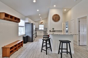 A modern kitchen with wooden shelves, a built-in refrigerator, and a large island with stools. - Rutland's Hidden Gem: 2 BR/1BA Renovated Home Close to Everything (Rutland)