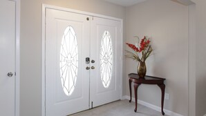 A hallway with a double door featuring stained glass designs, a small table with a vase of flowers, and a ceiling light fixture. - Lake view, Spacious 5 bedrooms, big lot, sleep 18 (Rockwall)