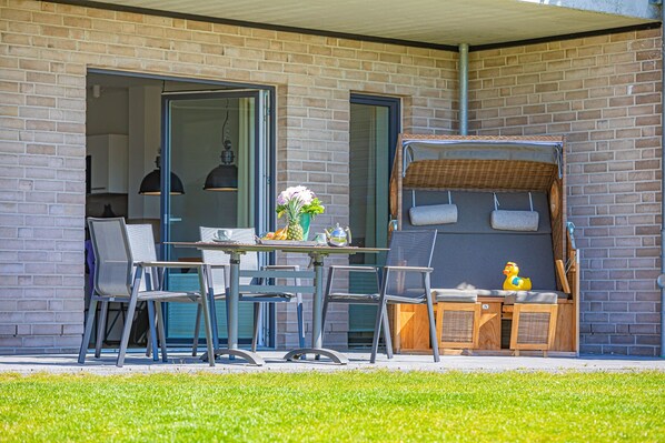 An outdoor patio with a table, chairs, and a wicker bench.