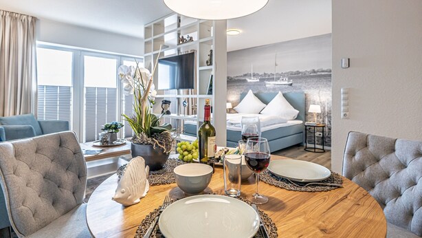 A dining area with a round table, chairs, a bottle of wine, and a vase of flowers.