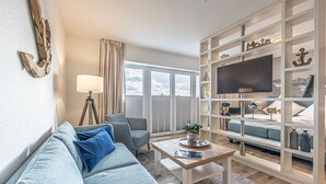 A living room with a grey sofa, a coffee table, and a TV on a white shelf.