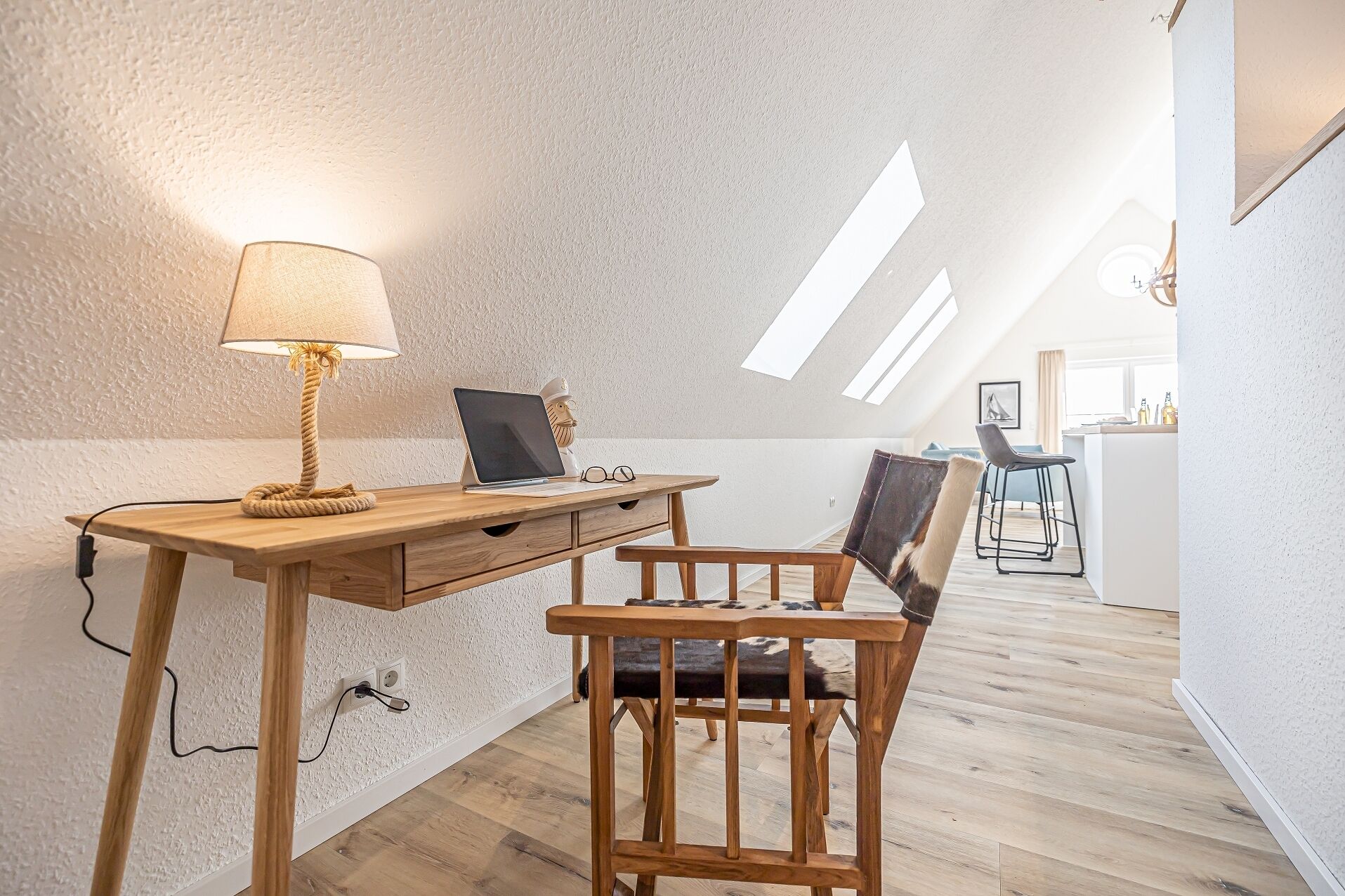 A cozy loft bedroom with a wooden desk, a chair, a lamp, and a laptop.