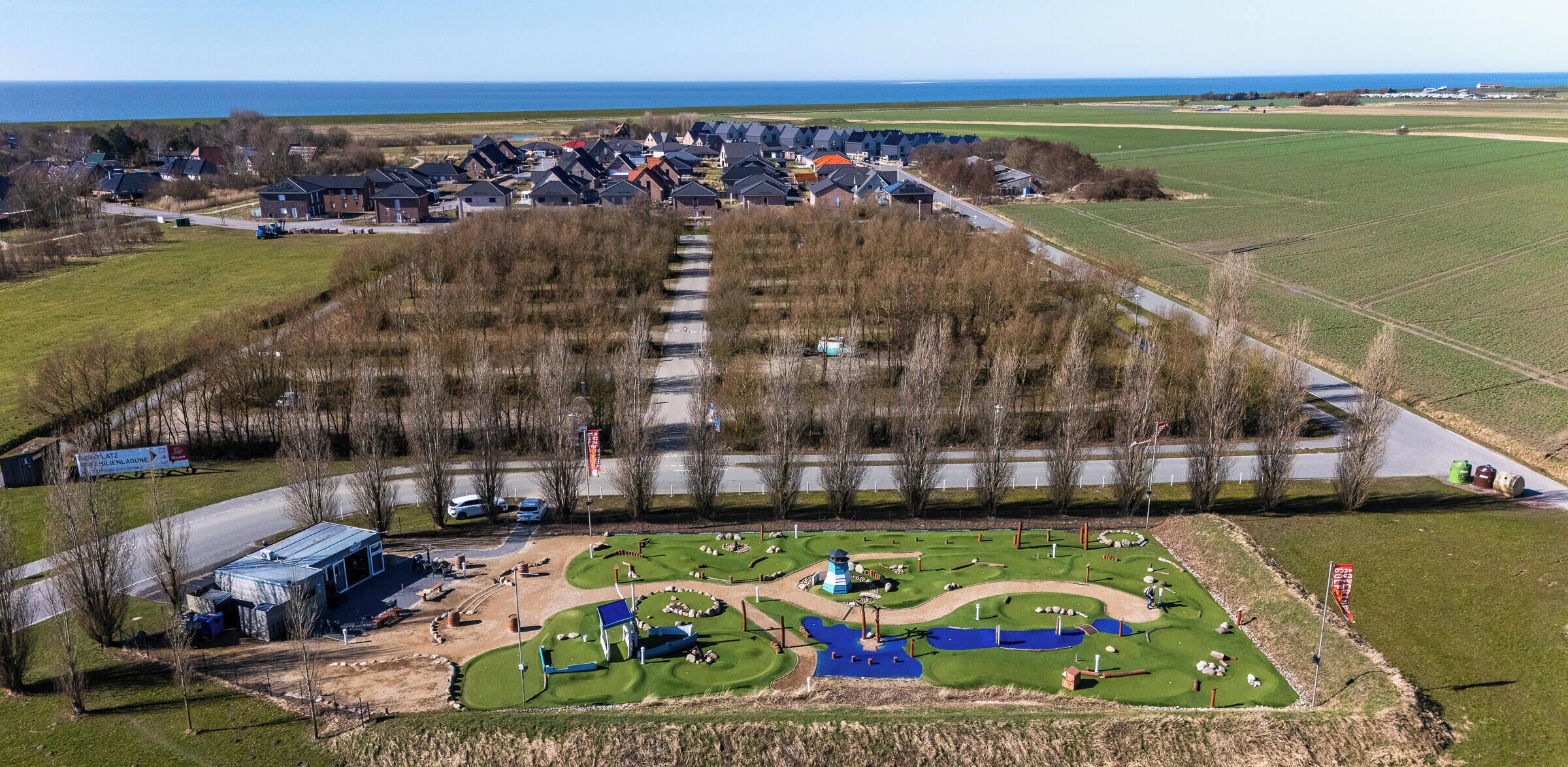 A golf course with a clubhouse, a pond, and a view of the sea.
