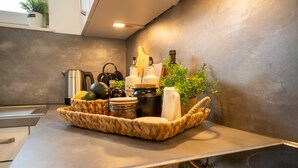 Una encimera de cocina con una cesta tejida que contiene utensilios de cocina, una tetera y botellas de aceite de oliva.