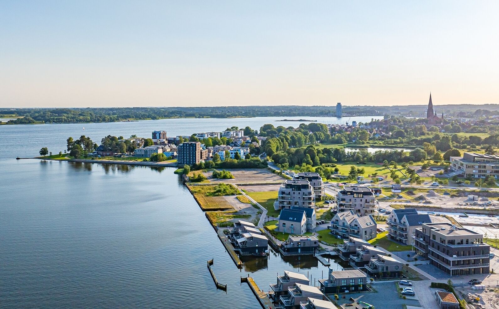 Luchtbeeld van een stad aan de rivier, met moderne gebouwen, een kerktoren en een jachthaven.