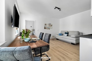 Uma sala de estar moderna com uma mesa de jantar de madeira, cadeiras estofadas cinzas, um sofá cinza e uma TV de tela plana fixada na parede.