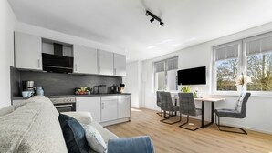 A modern kitchen with white cabinets, a black microwave, and a dining area with grey chairs and a wooden table.