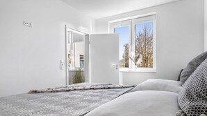 A bedroom with a bed, a window with a view of trees, and a door leading to another room.