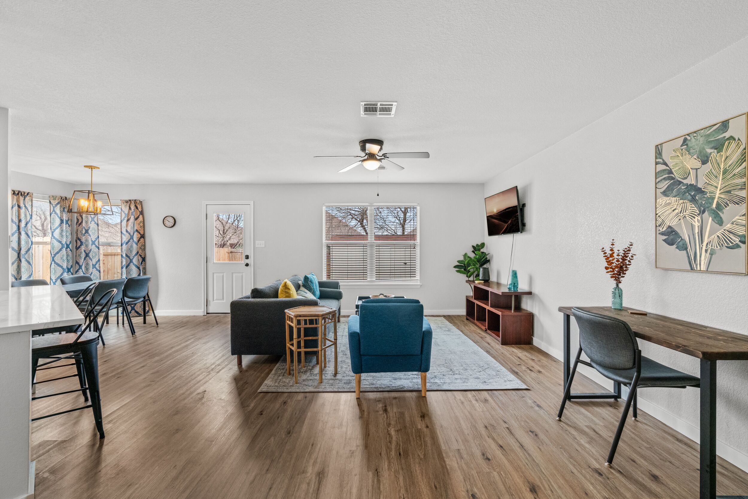 A spacious living area with a dining table, chairs, a sofa, and a TV mounted on the wall.