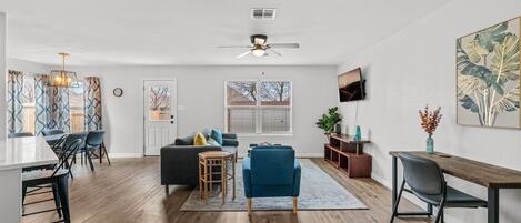 A spacious living area with a dining table, chairs, a sofa, and a TV mounted on the wall.