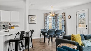 Una cuina moderna amb armaris blancs, un bar de cafè i una zona de menjador amb cadires i taula.