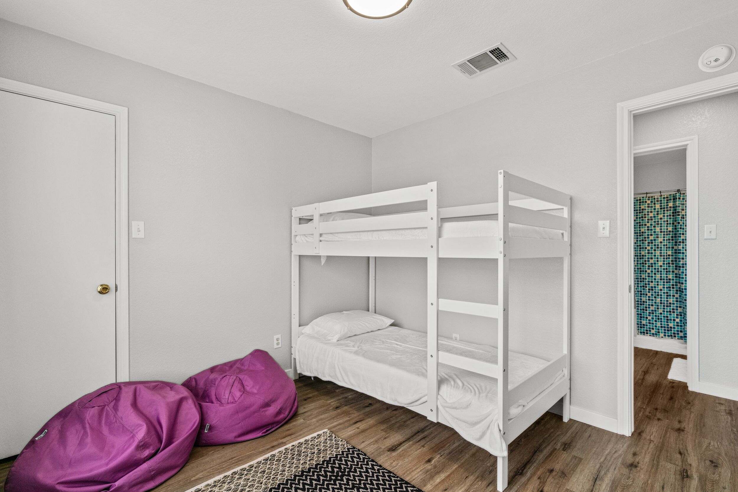 Une pièce avec un lit superposé, une porte, un tapis à motifs et une zone de douche carrelée.