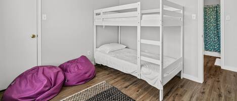 Une pièce avec un lit superposé, une porte, un tapis à motifs et une zone de douche carrelée.