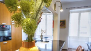 A modern kitchen with a central island, a vase with dried plants, and leather bar stools.