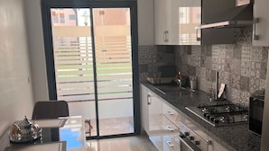 Une cuisine moderne équipée d’une cuisinière à gaz, d’un four et d’un four à micro-ondes. On y trouve une table à manger avec des chaises, ainsi qu’une porte-fenêtre coulissante donnant sur un espace extérieur.