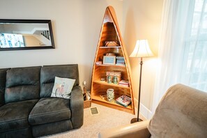 Un salon avec un canapé marron foncé, une bibliothèque en bois, un lampadaire et une fenêtre ornée de rideaux légers.