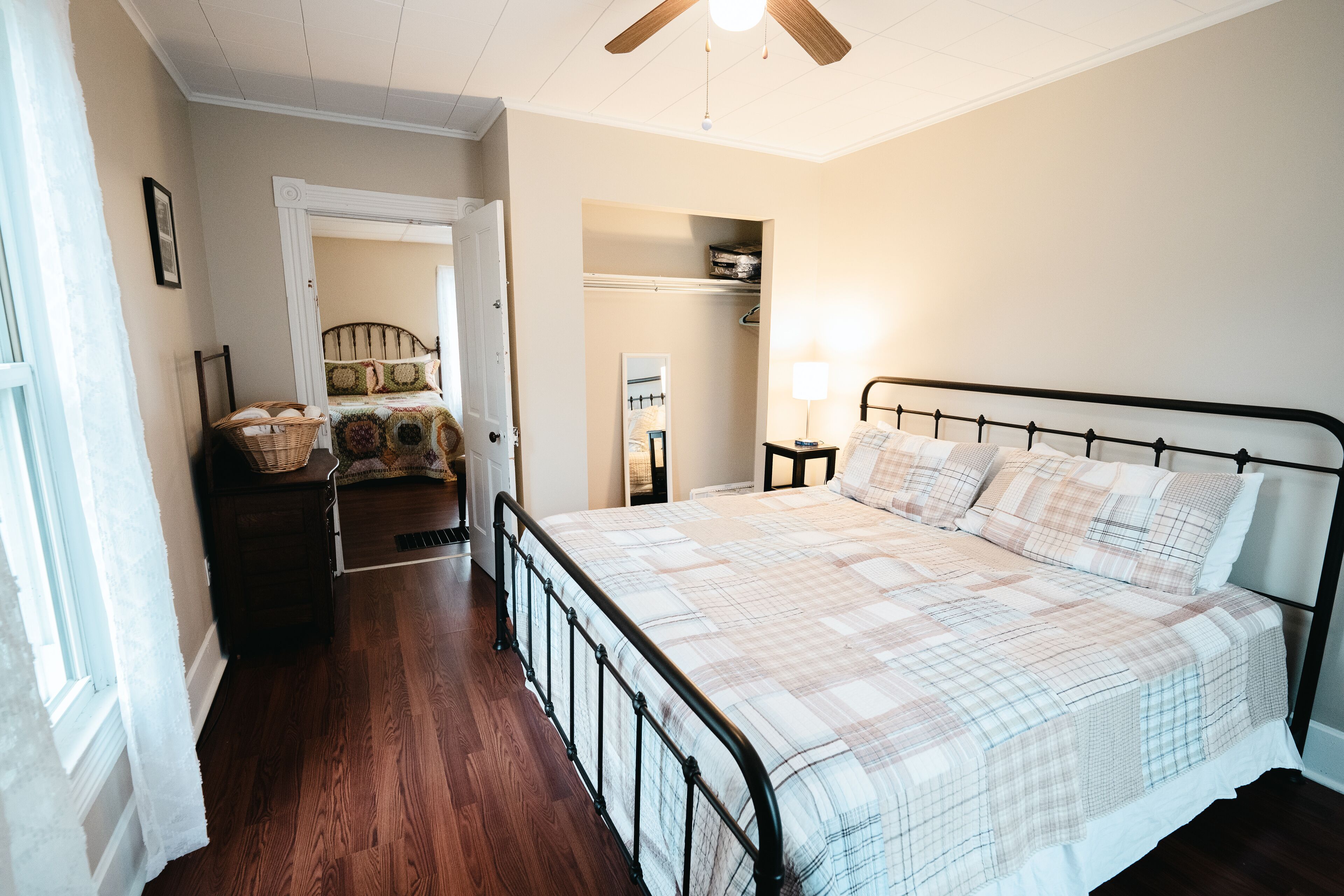 A bedroom with a large bed, a wooden floor, a ceiling fan, and a closet with a mirror.