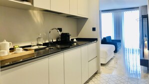 A modern kitchen with white cabinets, a black countertop, and a microwave. There is a sink with a faucet, and a coffee maker on the counter. A bed with a blue headboard is visible in the background. - Downtown 2C in Oporto (Porto)