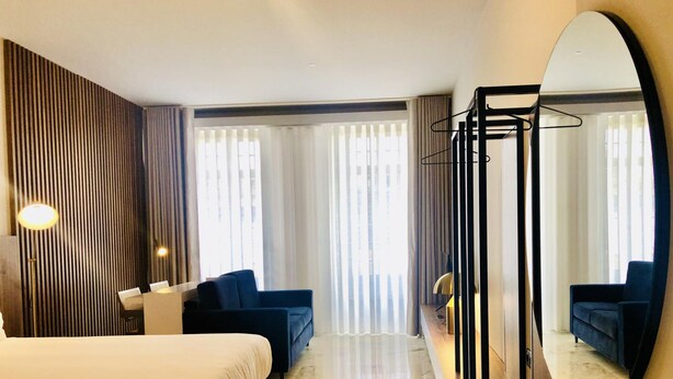 A hotel room with a bed, two armchairs, a desk, a mirror, and a view of the outside through large windows. - Downtown 2C in Oporto (Porto)