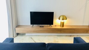 A modern living room with a flat-screen TV on a wooden stand, a gold table lamp, and dark blue sofas. - Downtown 2C in Oporto (Porto)