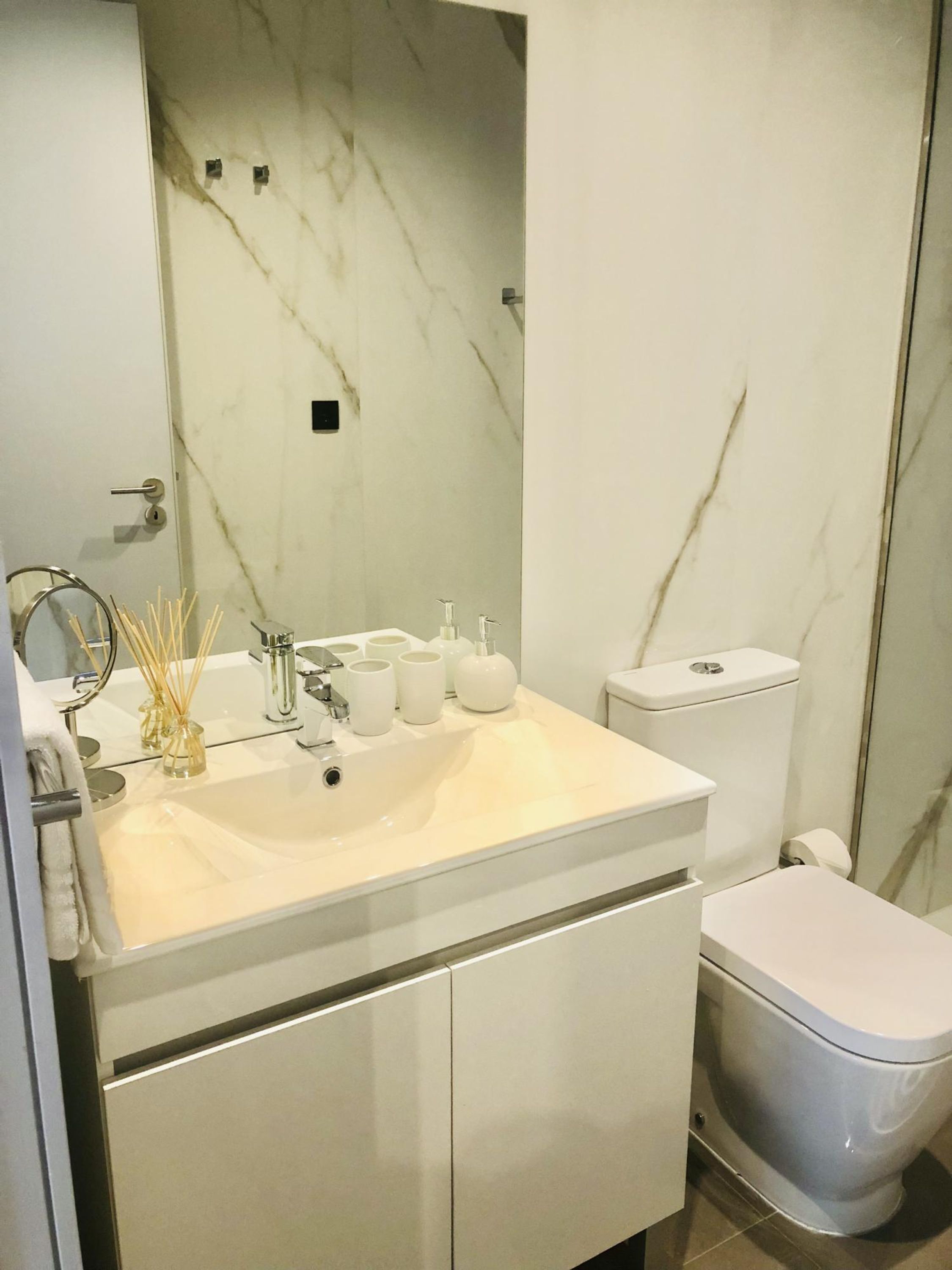 Ein modernes Badezimmer mit Marmorverkleidung, einem weißen Waschbecken und einer Toilette.