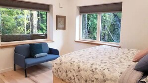 A bedroom with a bed, a blue sofa, and two windows with blinds. - Rainforest Lane Loft suite (Ucluelet)