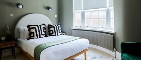 A bedroom with a bed, a window, a radiator, and a green chair.