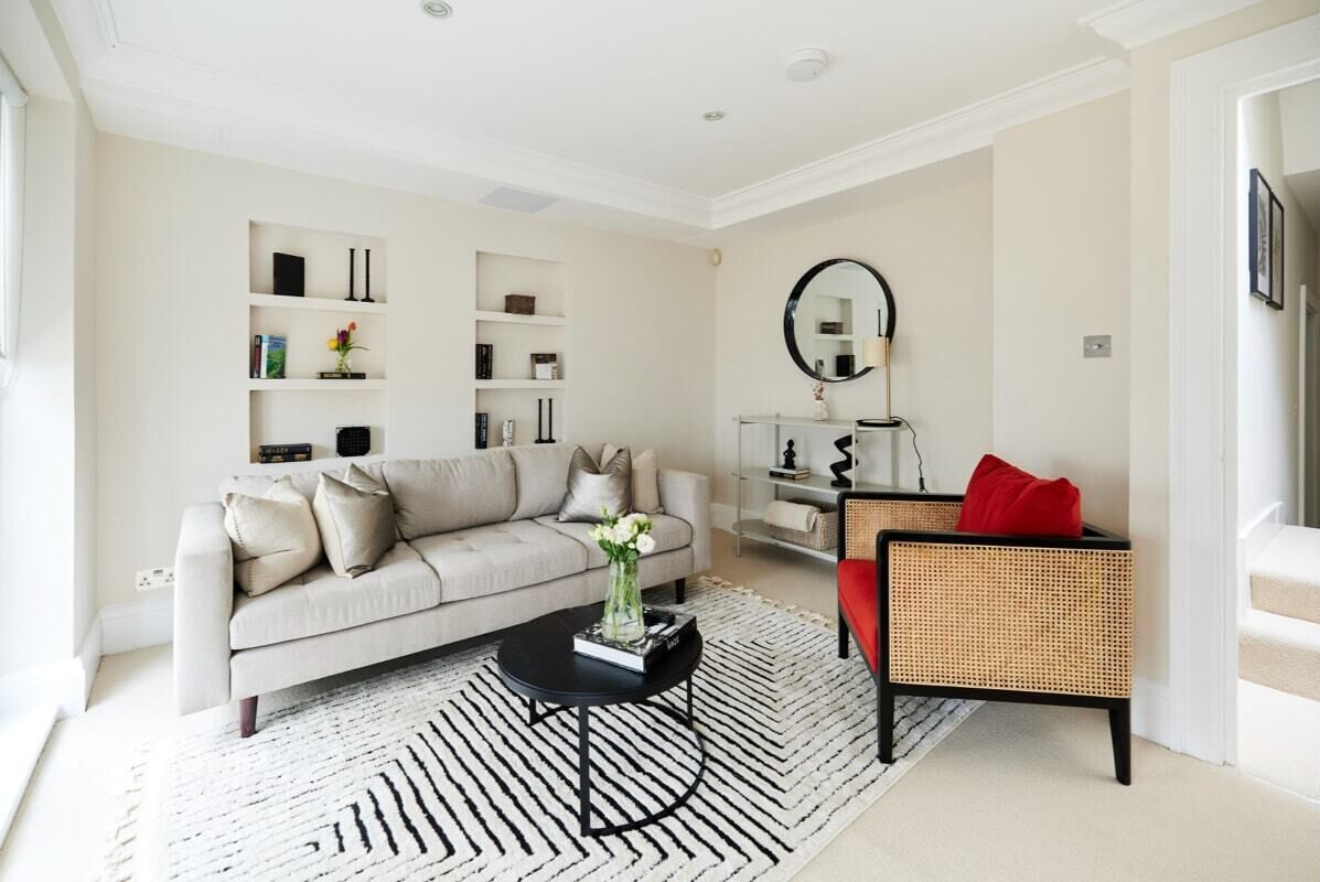 A modern living room with a sofa, a coffee table, a rattan chair, a bookshelf, and a mirror.