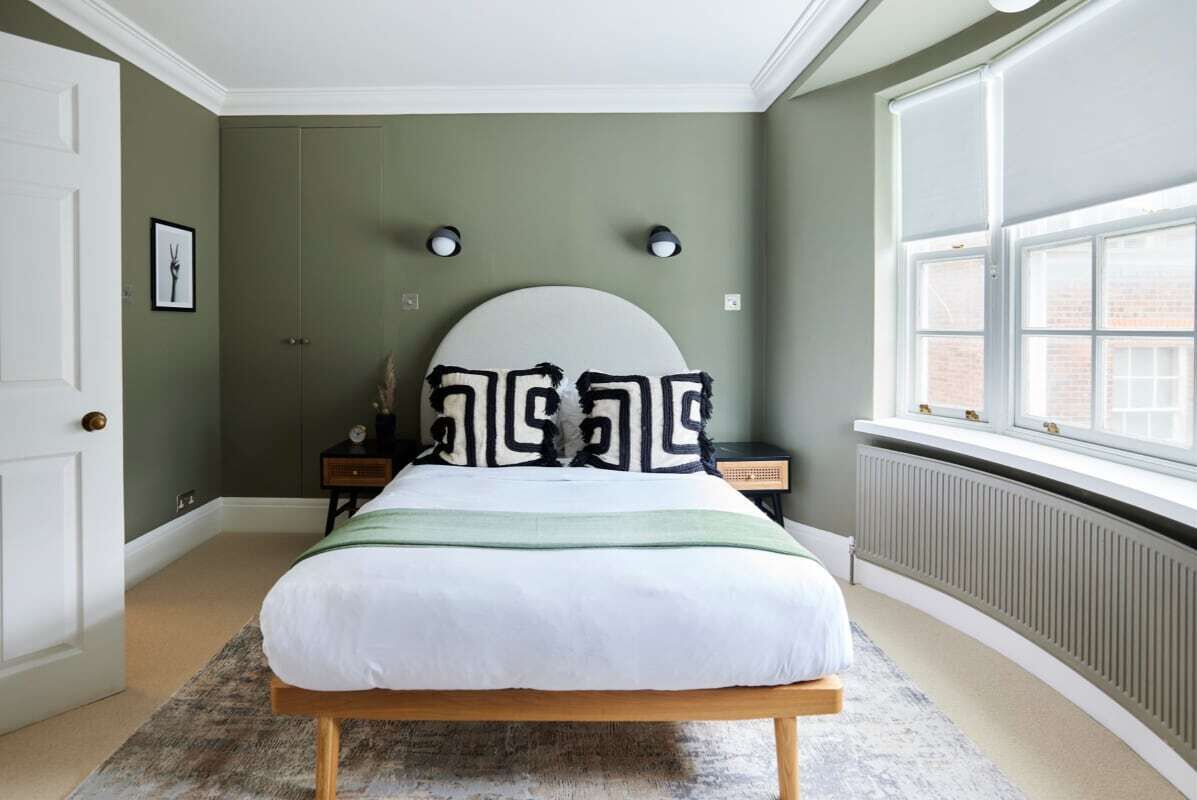 A bedroom with a bed, a nightstand, a dresser, a window, and a radiator.