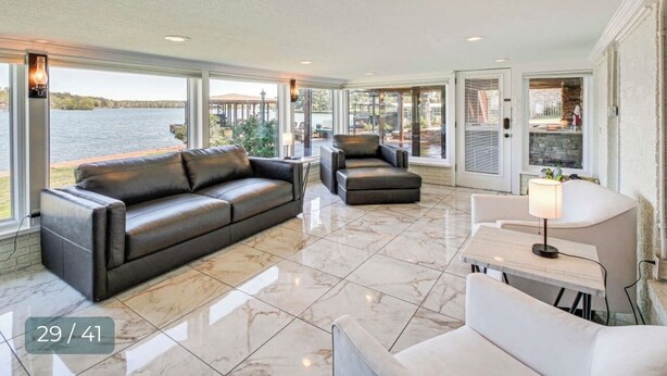 A spacious living area with a large window overlooking a body of water, a leather sofa, a white table, and a chair. -  Modern Lakefront Property
 (Hot Springs)