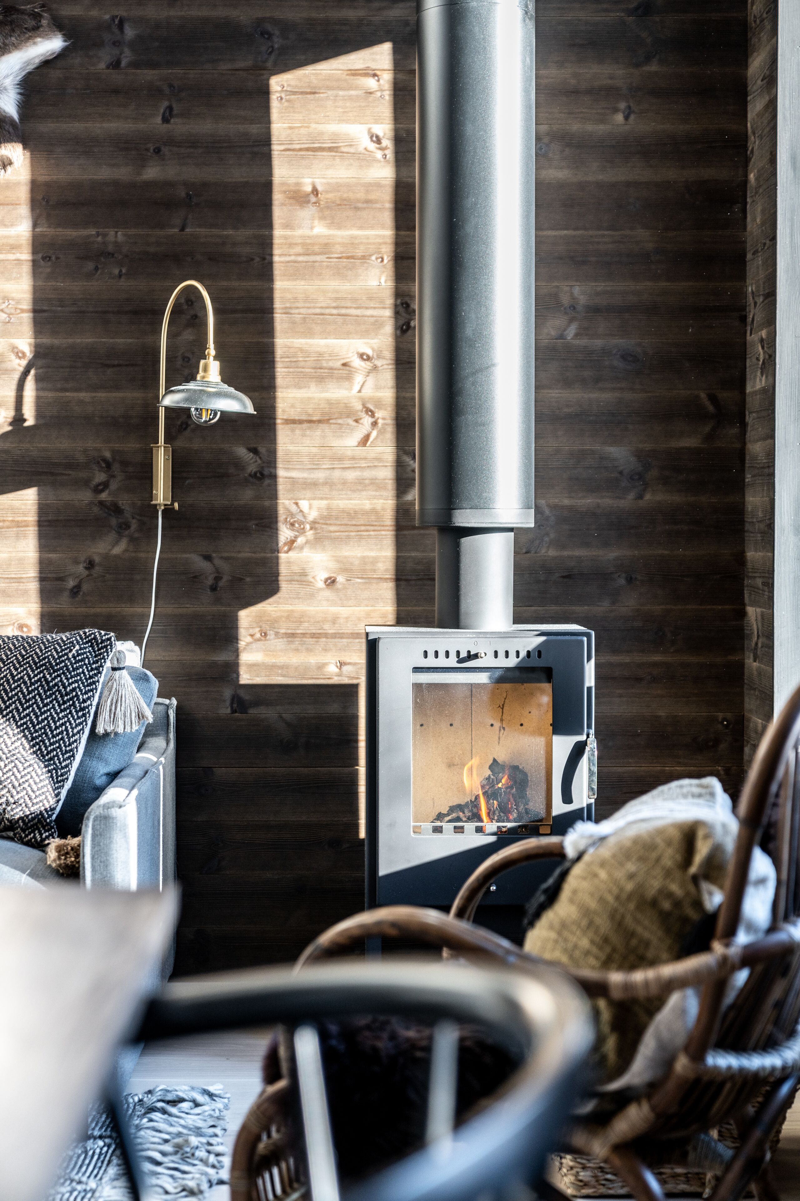 A cozy room with a wood-burning stove, a hanging lamp, and wicker furniture.