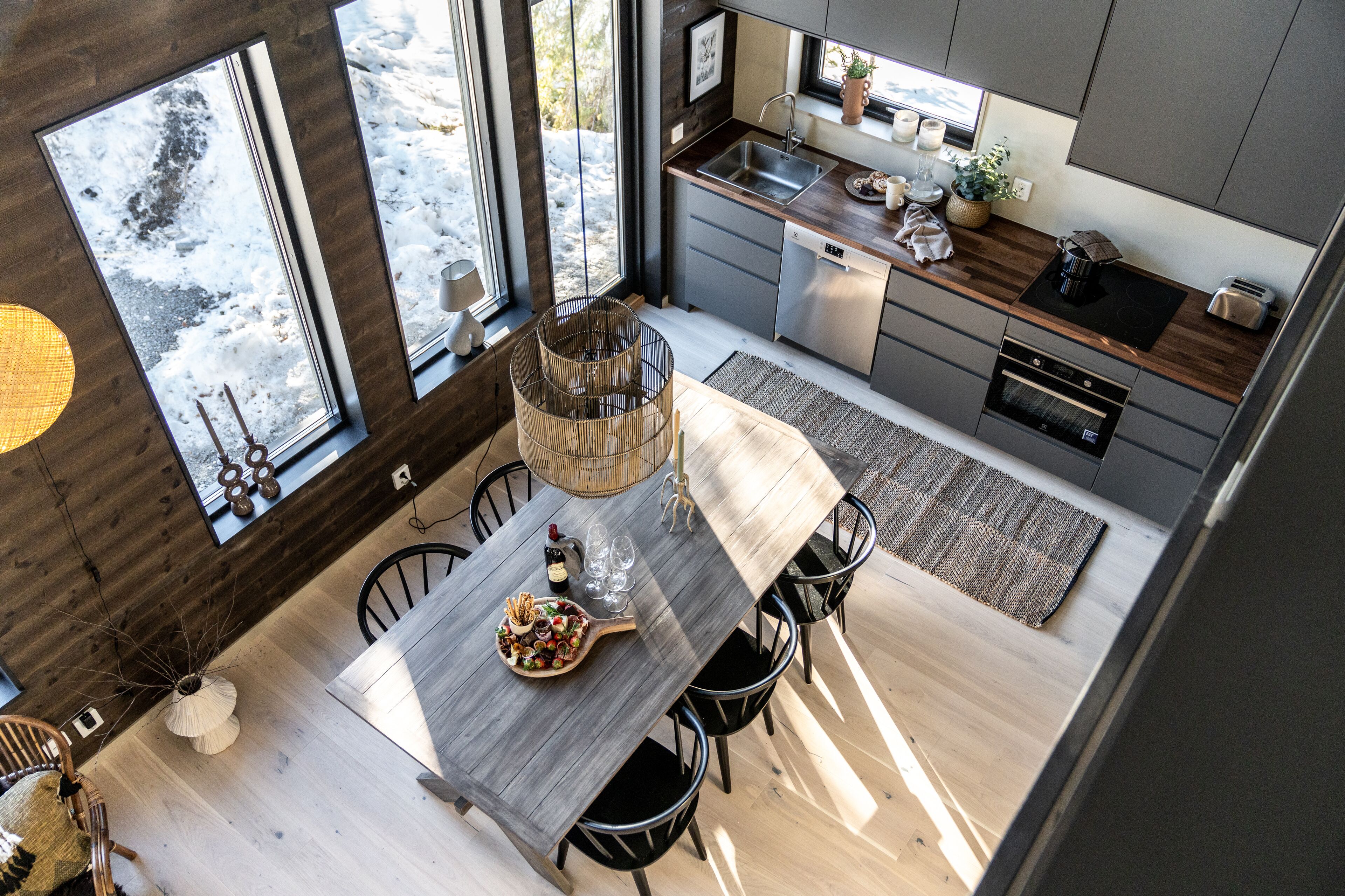 A modern kitchen with a wooden dining table, chairs, and a view of the snowy outdoors.