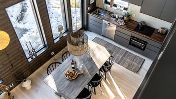 A modern kitchen with a wooden dining table, chairs, and a view of the snowy outdoors.