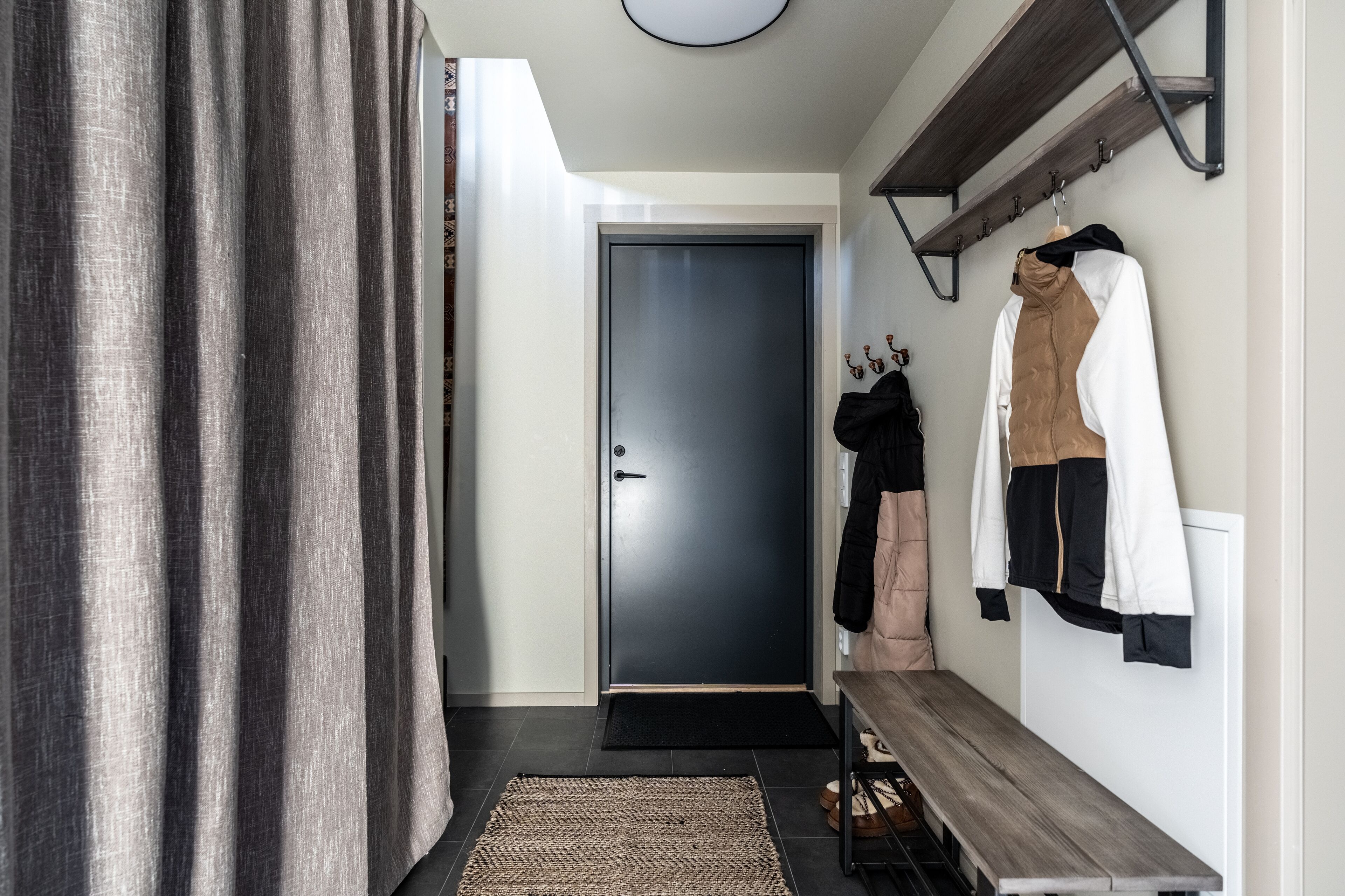 A hallway with a dark door, a bench, and a coat rack with jackets.
