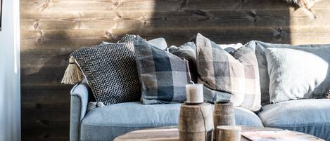 A cozy living room with a wooden wall, a fur rug, and a sofa with cushions.
