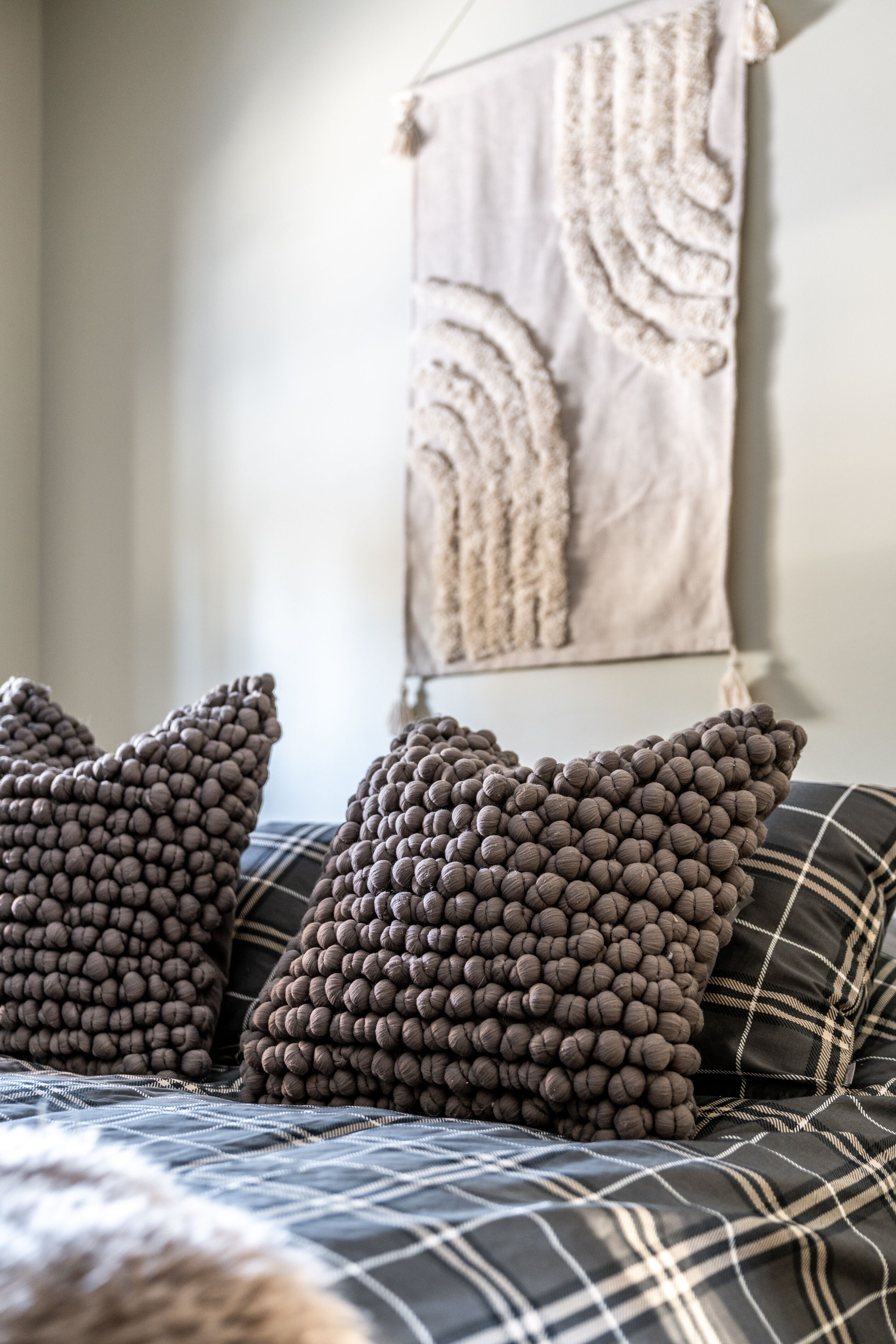 A bed with a plaid bedspread and three textured pillows.