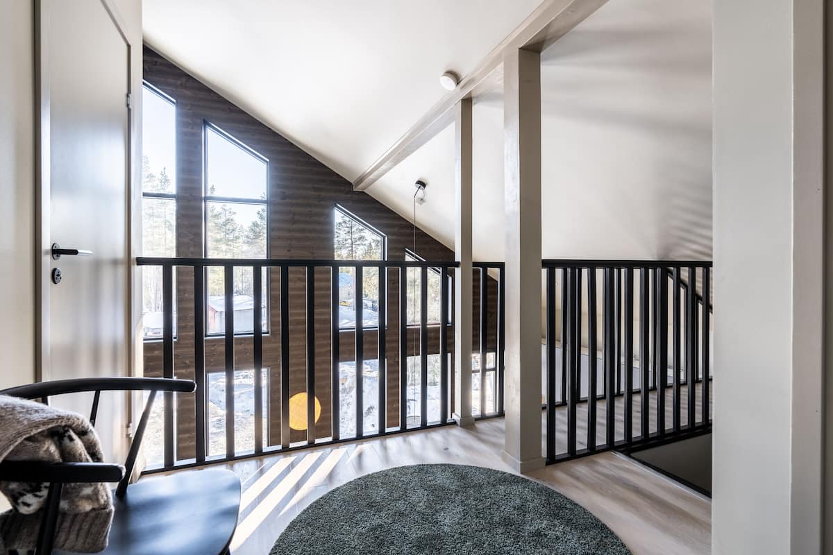 A modern interior with a view to a balcony, a staircase, and a seating area with a rug.