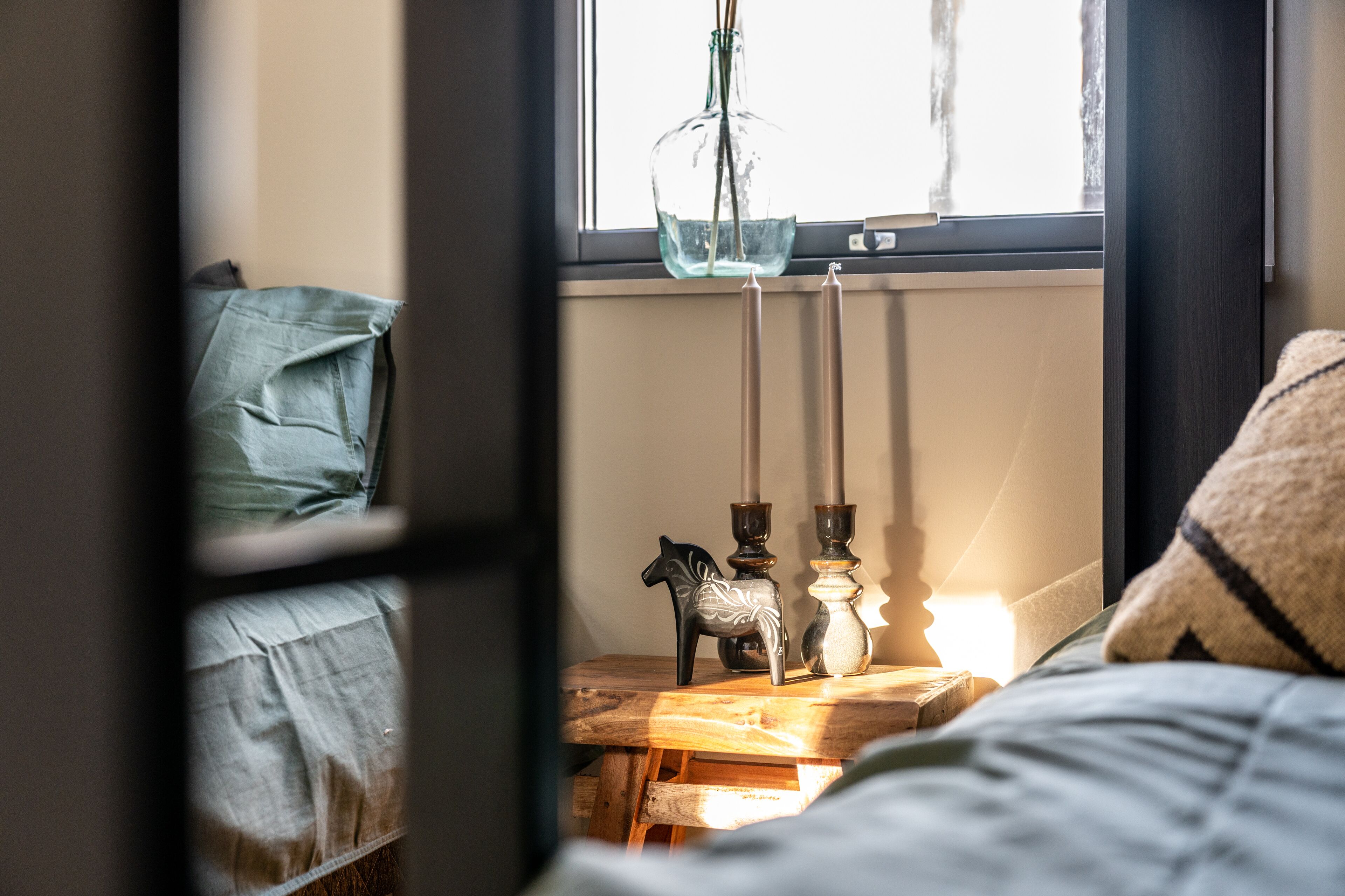 A bedroom with a bed, a bedside table with candles, and a window with a view.