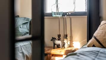 A bedroom with a bed, a bedside table with candles, and a window with a view.