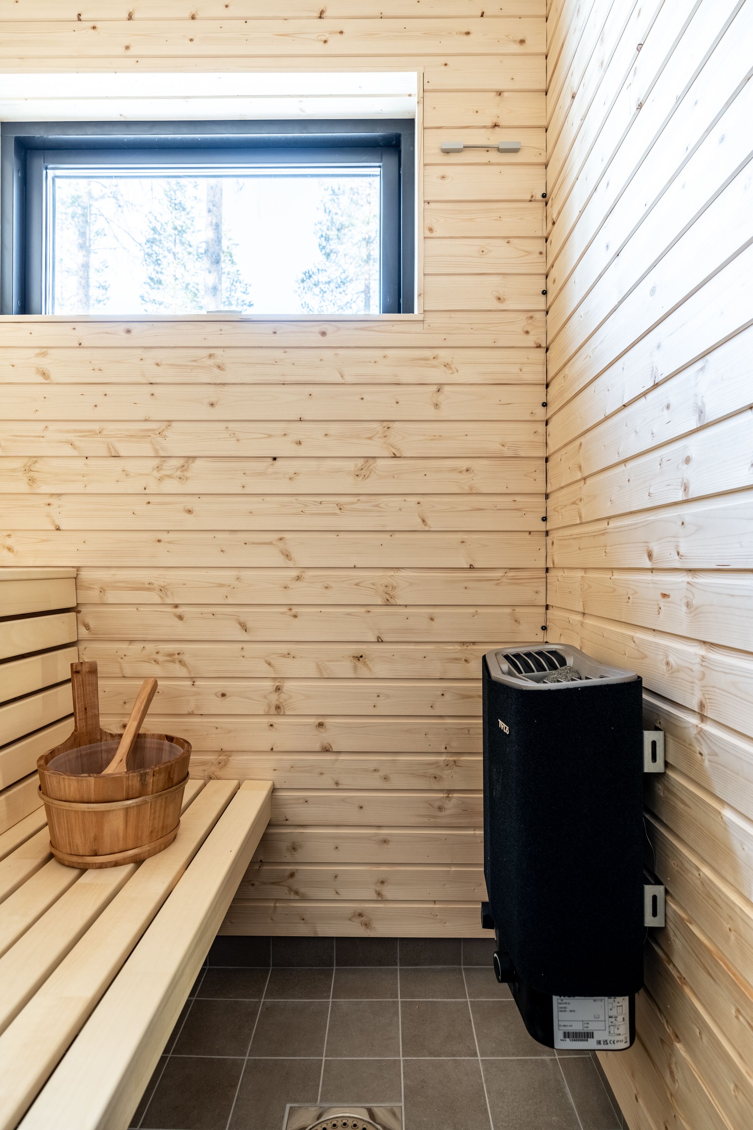 A sauna room with wooden benches, a window, and a sauna heater.