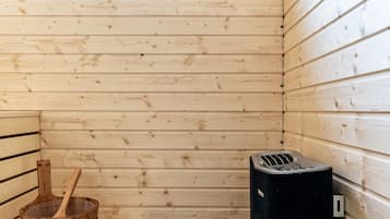A sauna room with wooden benches, a window, and a sauna heater.