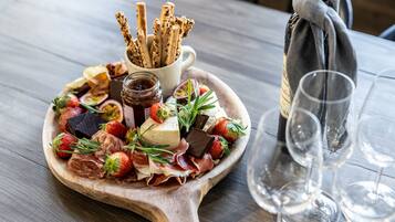A wooden board with assorted cheeses, strawberries, and prosciutto, accompanied by crackers and a bottle of wine.