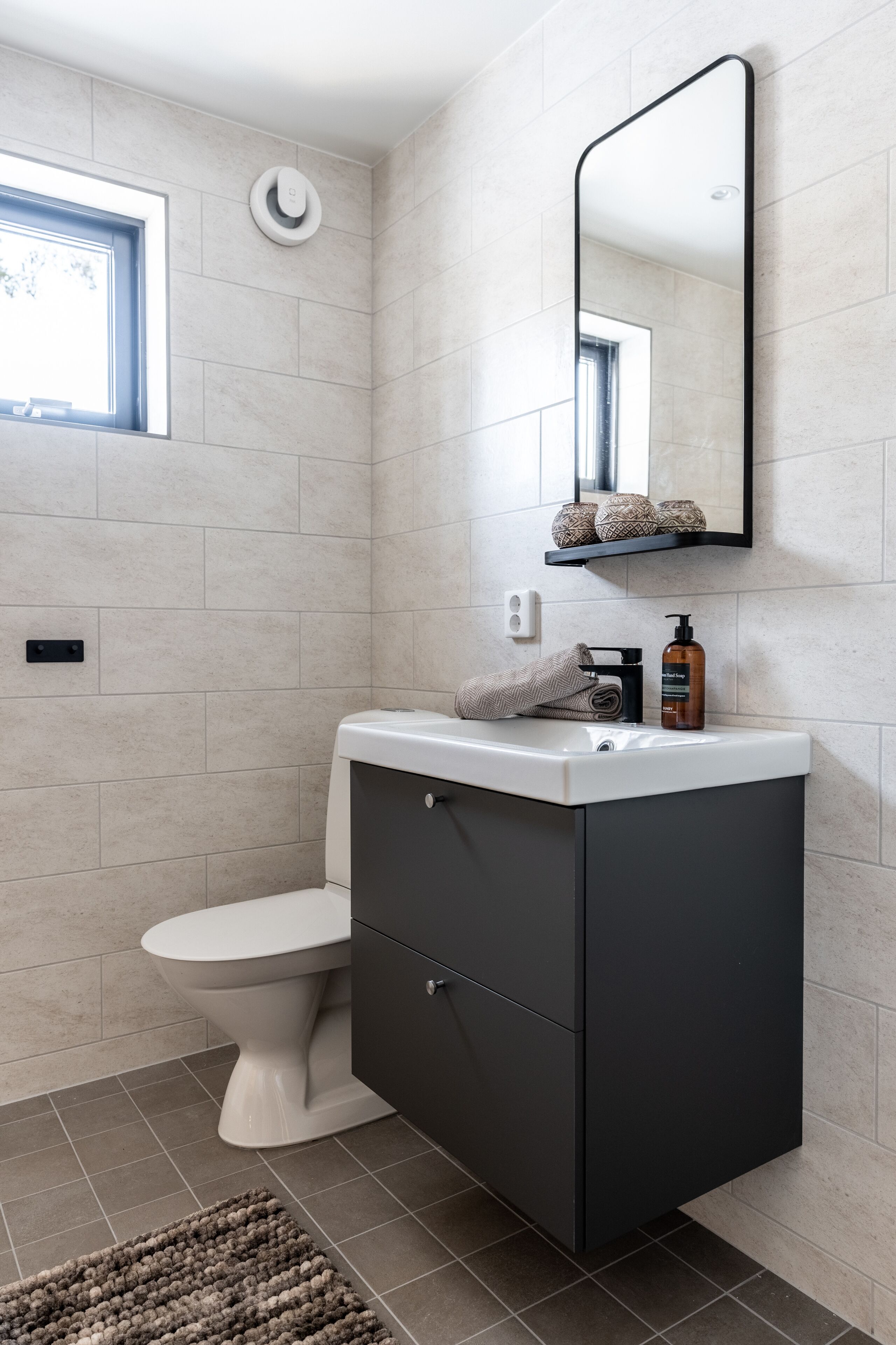 Un baño moderno con inodoro, tocador con espejo y ventana que proporciona luz natural.
