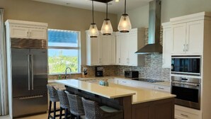 Uma cozinha moderna com ilha central, banquetas, eletrodomésticos de aço inoxidável e iluminação pendente.