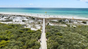 A beach with a clear path leading to the shore, a flag, and a sandy area with sparse vegetation. - Inlet Beach Dream - East 30A, Gulf View, Near Shops + Dining, Steps to the Sand! (Inlet Beach)