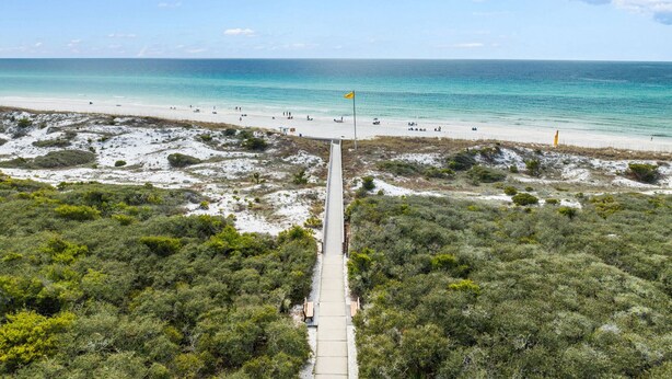 A beach with a clear path leading to the shore, a flag, and a sandy area with sparse vegetation.