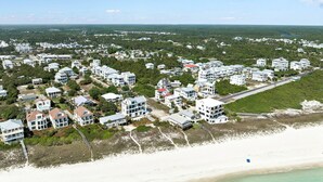 An aerial view of a coastal residential area with multiple white buildings, a beach, and a clear sky.