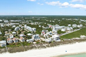 Vue aérienne d’un quartier résidentiel situé sur la côte, avec de nombreux bâtiments blancs, une plage et un ciel dégagé.