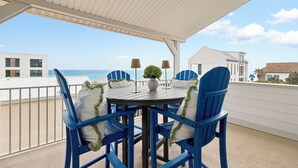 A covered outdoor seating area with a table and chairs, overlooking a beach.